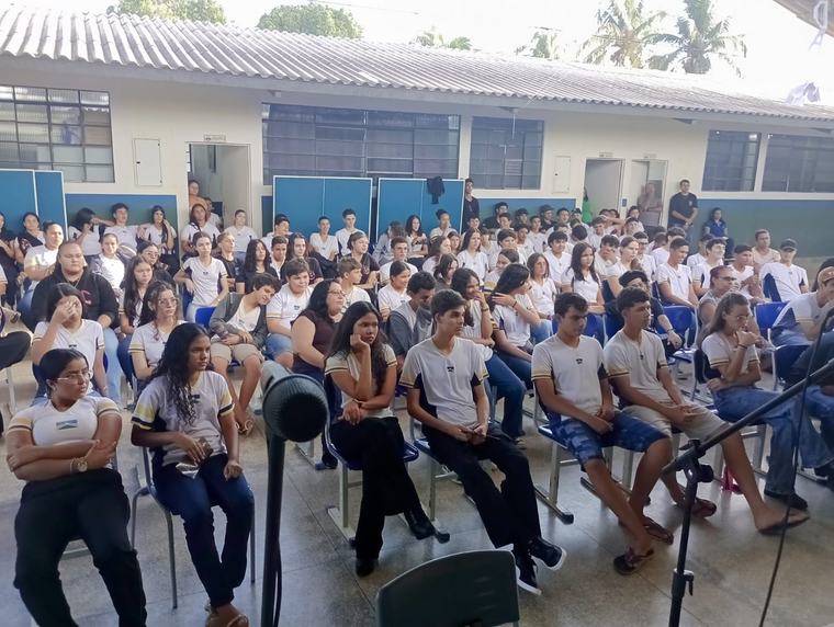 Pátio de escola lotado de alunos de uniforme assistindo a uma apresentação do coletivo.