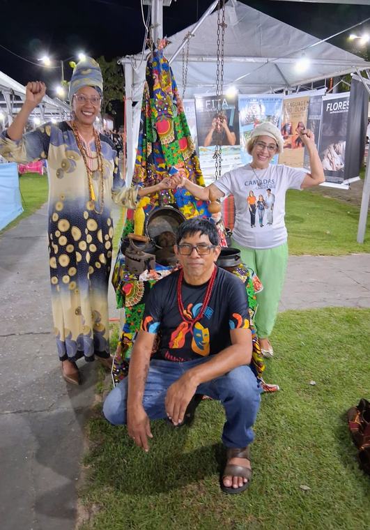 Artistas de figurino colorido num evento ao ar livre, à noite, com tendas ao fundo.