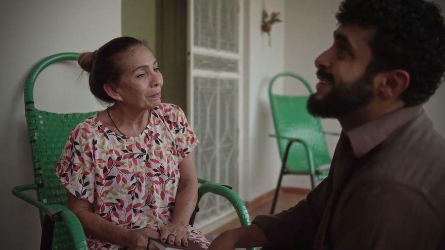 Cena do filme Fita: uma senhora numa cadeira de varanda verde conversa com um homem de barba.