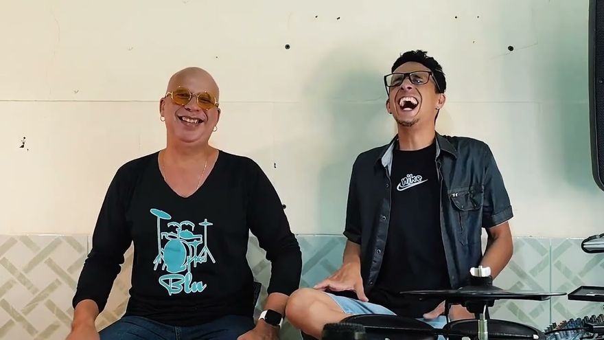 Cena do documentário Olhares: dois músicos rindo, sentados diante de uma bateria.