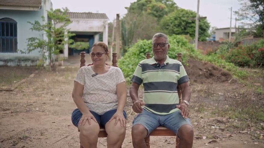 Cena do documentário Deus, eu e o cachorro Totó: um casal sentado lado a lado num quintal de terra.